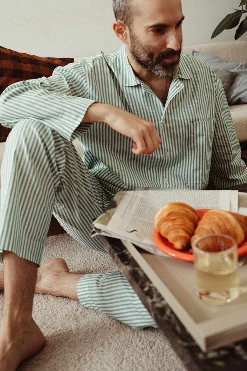 guy in striped pyjamas is sitting on the ground with newspapers and croissants