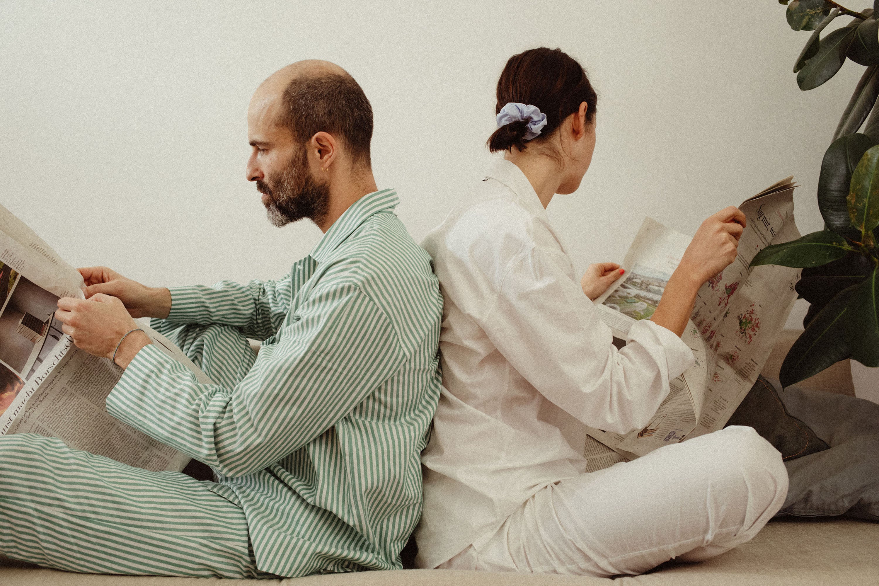 couple in Pyjamas is sitting on a sofa reading newspaper