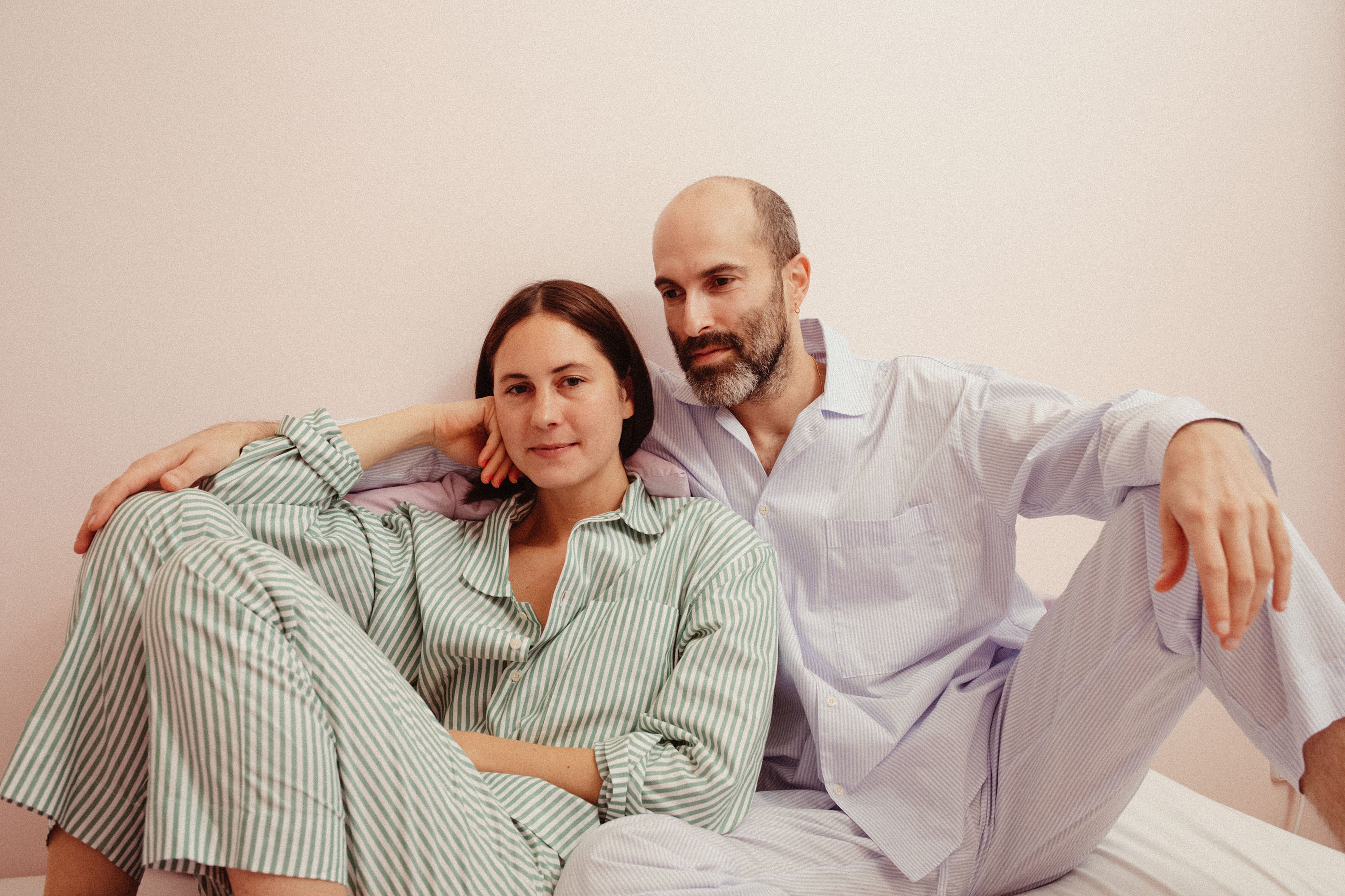 couple wearing long pyjama sets in different stripes, while sitting in bed