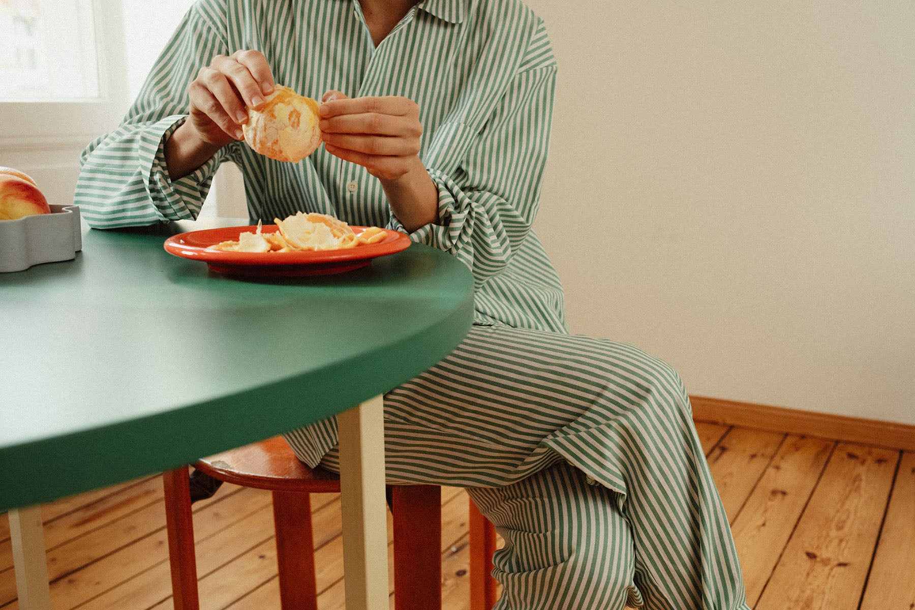 A woman in striped pyjamas is sitting at a table, peeling oranges
