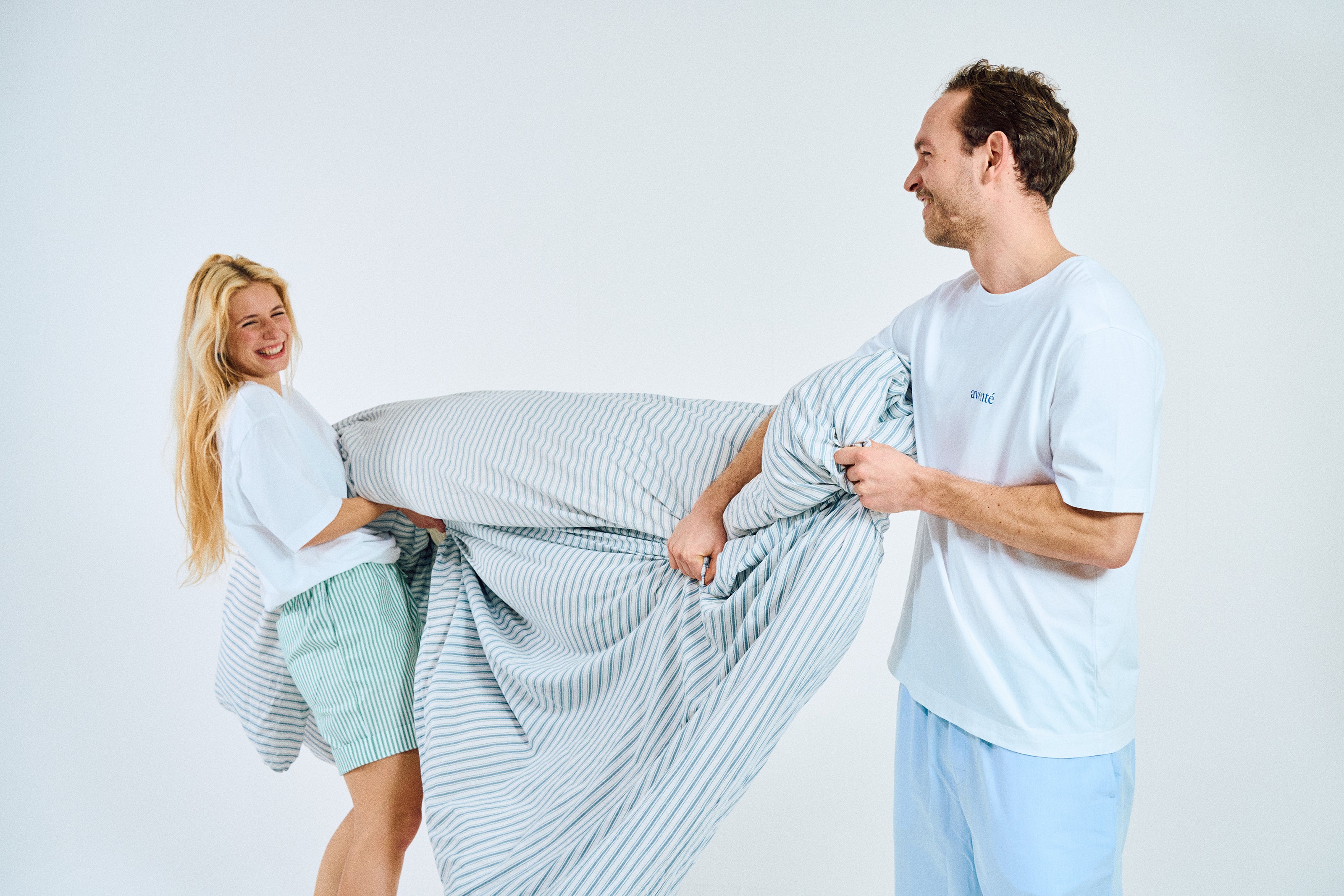 couple in sustainable sleepwear fighting with blanket