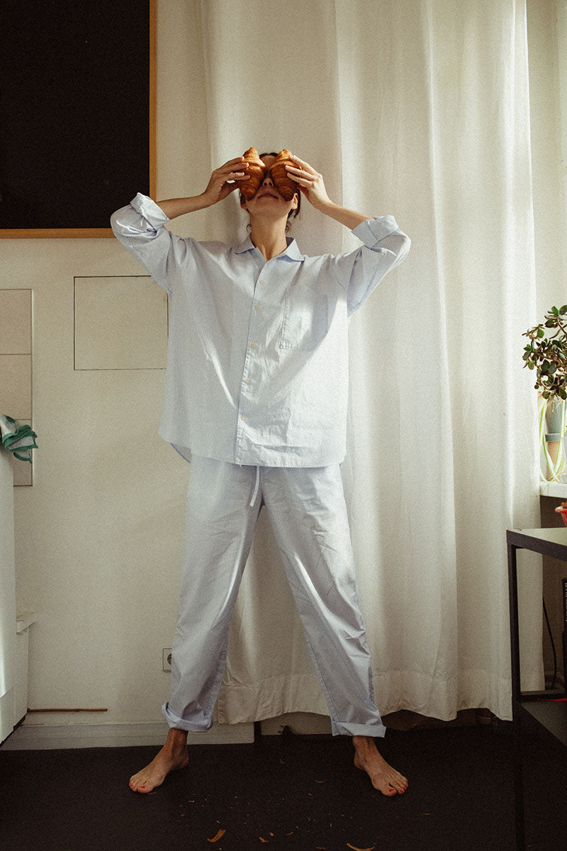 a women in sustainable pyjamas is standing in her kitchen, holding two croissants in front of her face