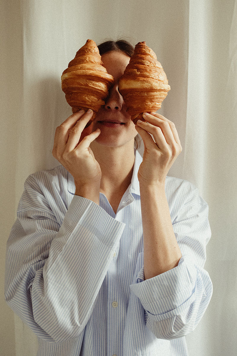 woman in a sustainable pyjama shirt with two Croissants in front of her face
